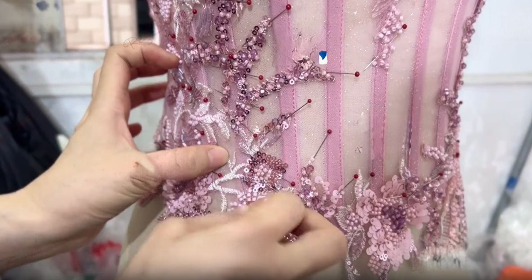 Dressmaker pinning floral appliques onto pink tulle gown during prom dress construction