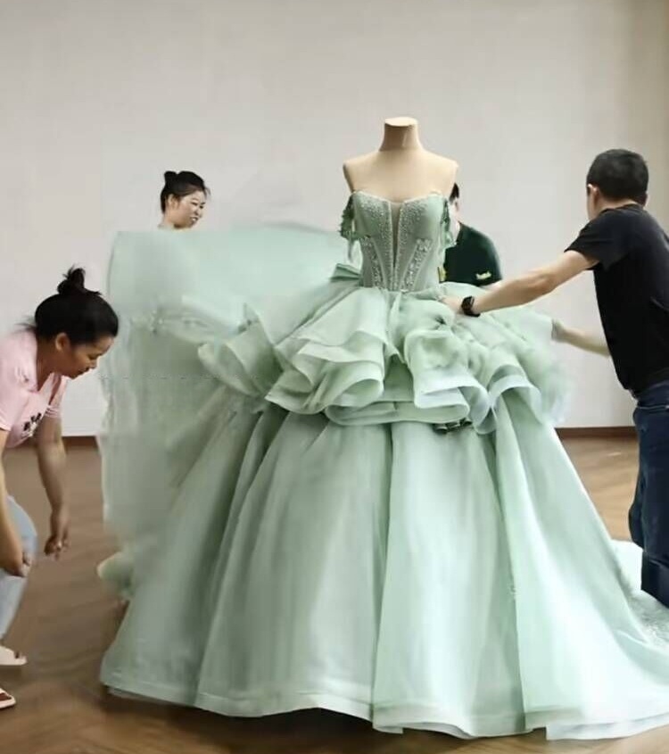 The team putting the finishing touches on the final assembly of the massive mint green gown on the mannequin, adjusting the ruffled skirt and bodice. The team putting the finishing touches on the final assembly of the massive mint green gown on the mannequin, adjusting the ruffled skirt and bodice.