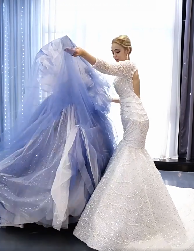 Model wearing a fitted white beaded mermaid gown with a large blue and white sparkle tulle overskirt and dramatic train Model wearing a fitted white beaded mermaid gown with a large blue and white sparkle tulle overskirt and dramatic train