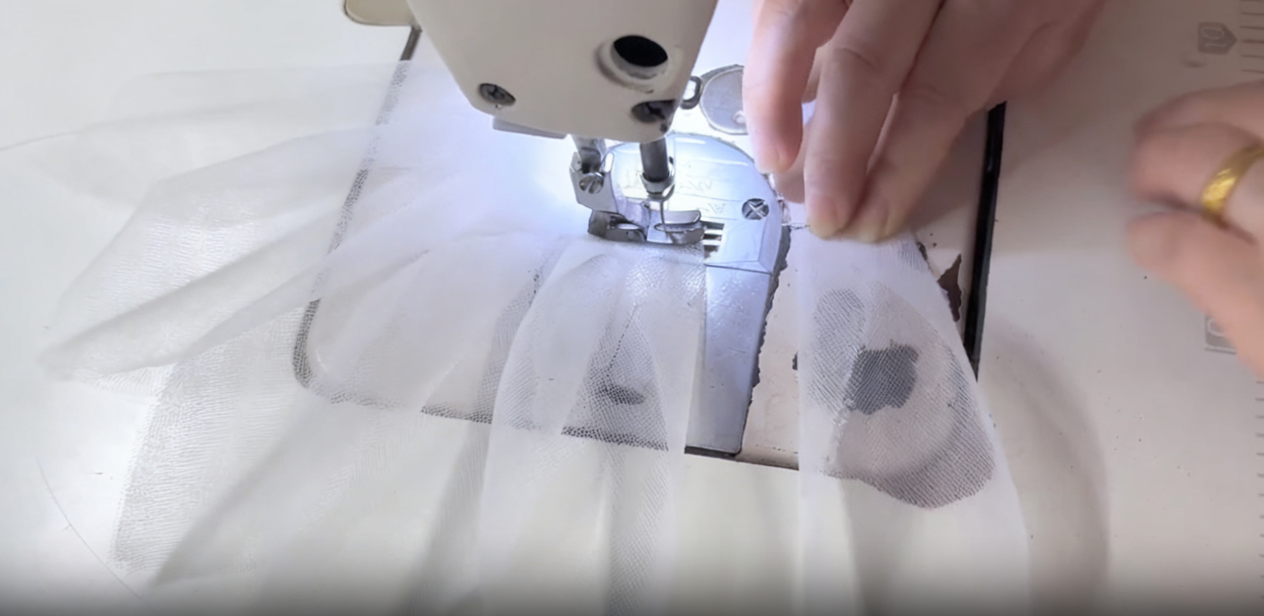 Hands guiding white tulle layers through an industrial sewing machine while creating a custom wedding or formal gown Hands guiding white tulle layers through an industrial sewing machine while creating a custom wedding or formal gown
