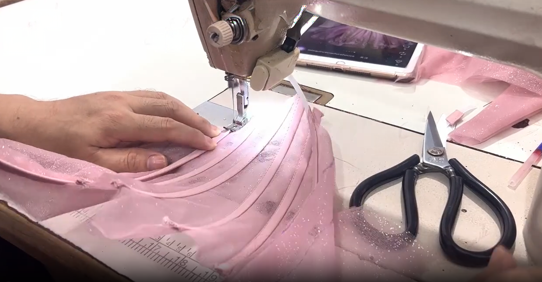 A tailor sewing pink glitter fabric with an industrial Juki machine for a handmade gown