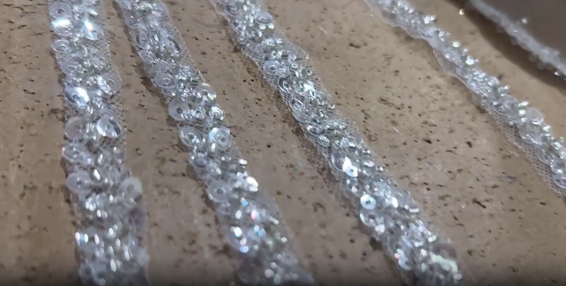 A seamstress using a sewing machine to stitch heavily sequined fabric onto plain white backing fabric, creating the bodice of the dress. A seamstress using a sewing machine to stitch heavily sequined fabric onto plain white backing fabric, creating the bodice of the dress.