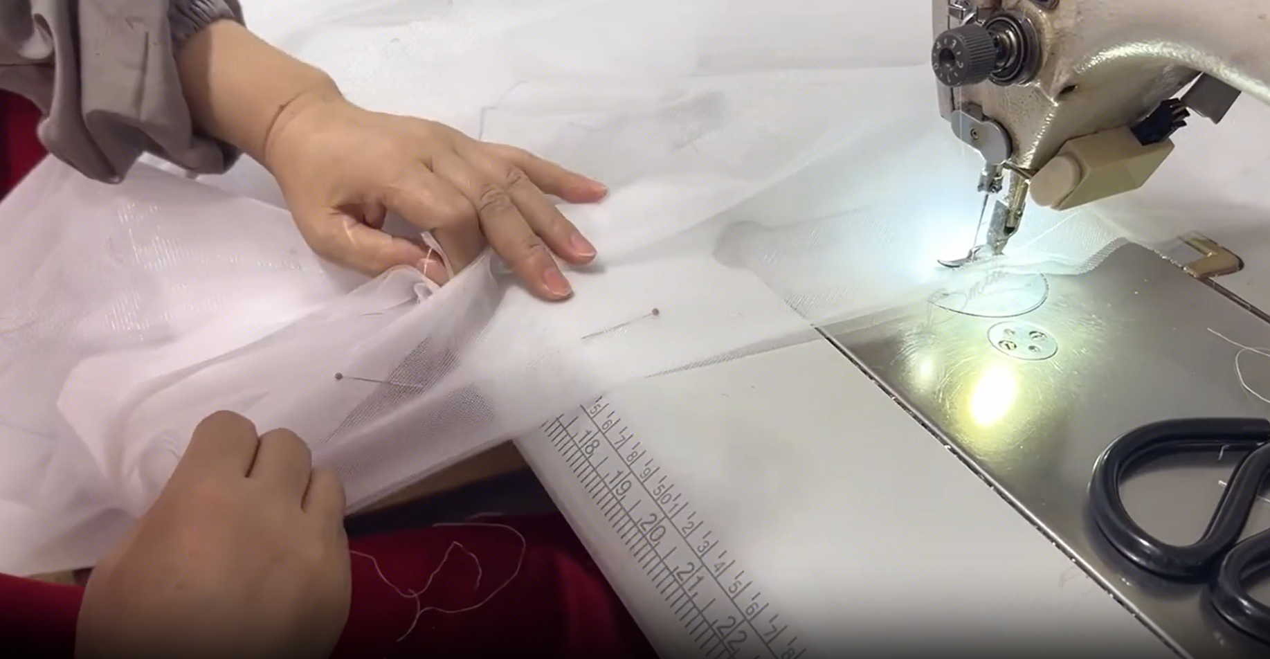 Sewing white sheer tulle fabric on an industrial sewing machine. Sewing white sheer tulle fabric on an industrial sewing machine.