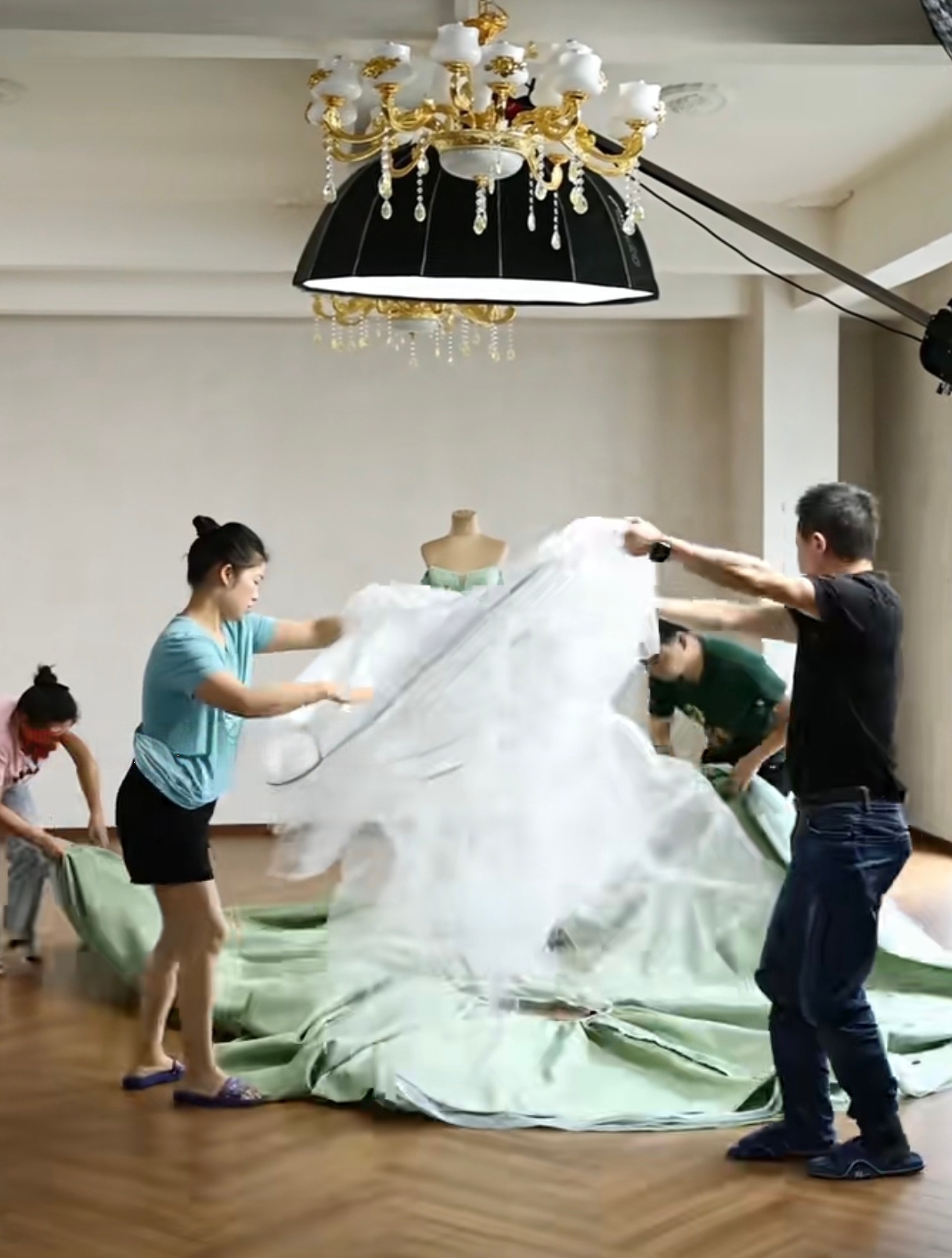 Two team members working together to lift and spread a large layer of white tulle over a massive circle of mint green fabric on the wooden floor. Two team members working together to lift and spread a large layer of white tulle over a massive circle of mint green fabric on the wooden floor.