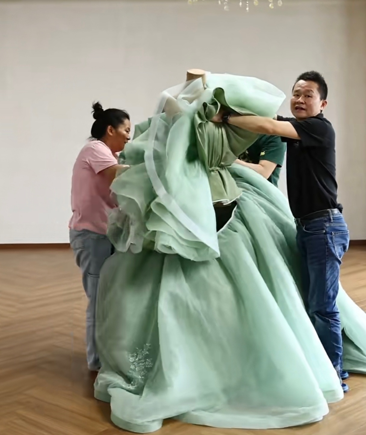 Two seamstresses arranging the cascading ruffles and large layers of the mint green ball gown around the mannequin. Two seamstresses arranging the cascading ruffles and large layers of the mint green ball gown around the mannequin.