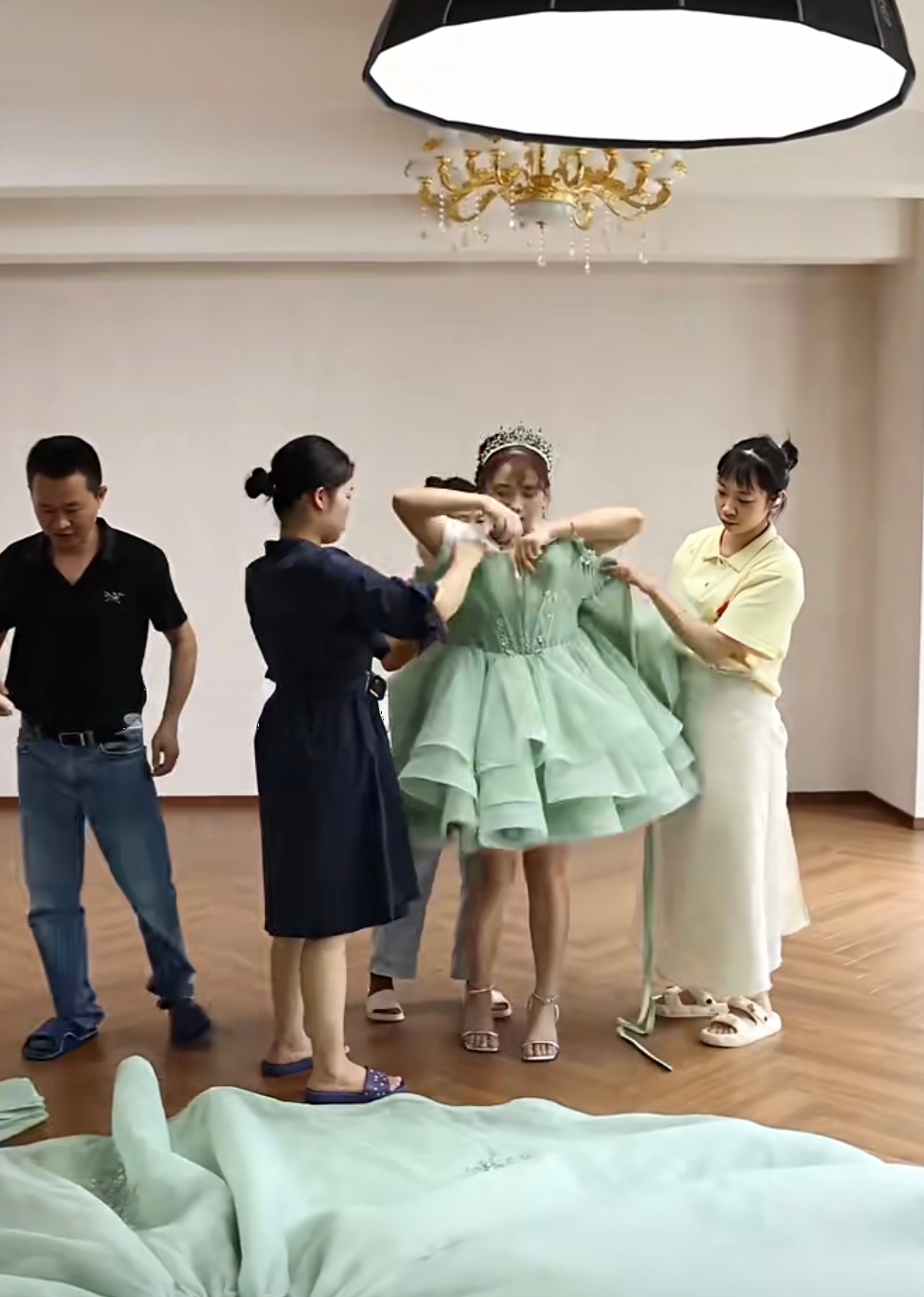 A model trying on the short mint green tiered dress, with three team members assisting her with the sleeves and hemline. A model trying on the short mint green tiered dress, with three team members assisting her with the sleeves and hemline.