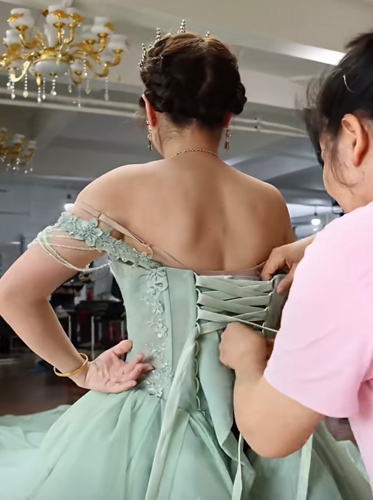 View from behind as a seamstress tightens the corset lace-up back of the mint green dress View from behind as a seamstress tightens the corset lace-up back of the mint green dress